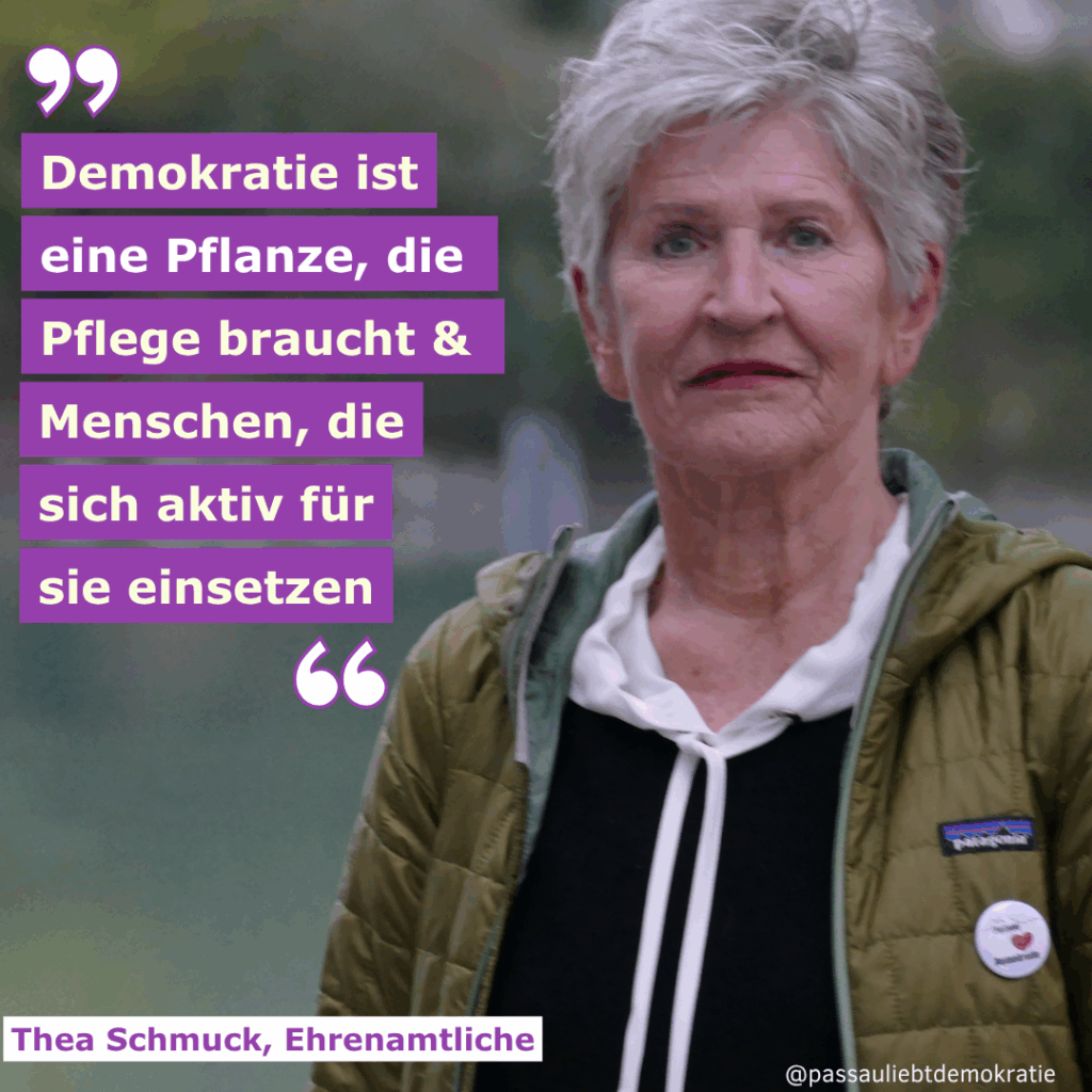 Das Bild zeigt ein Porträt von Thea Schmuck, einer Ehrenamtlichen bei "Omas gegen Rechts Passau". Sie hat kurzes, weißes Haar, trägt eine grüne Jacke und ein schwarzes Sweatshirt mit weißem Kragen. In Anführungszeichen steht das Zitat "Demokratie ist eine Pflanze, die Pflege braucht und Menschen, die sich aktiv für sie einsetzen." auf lila Grund.
