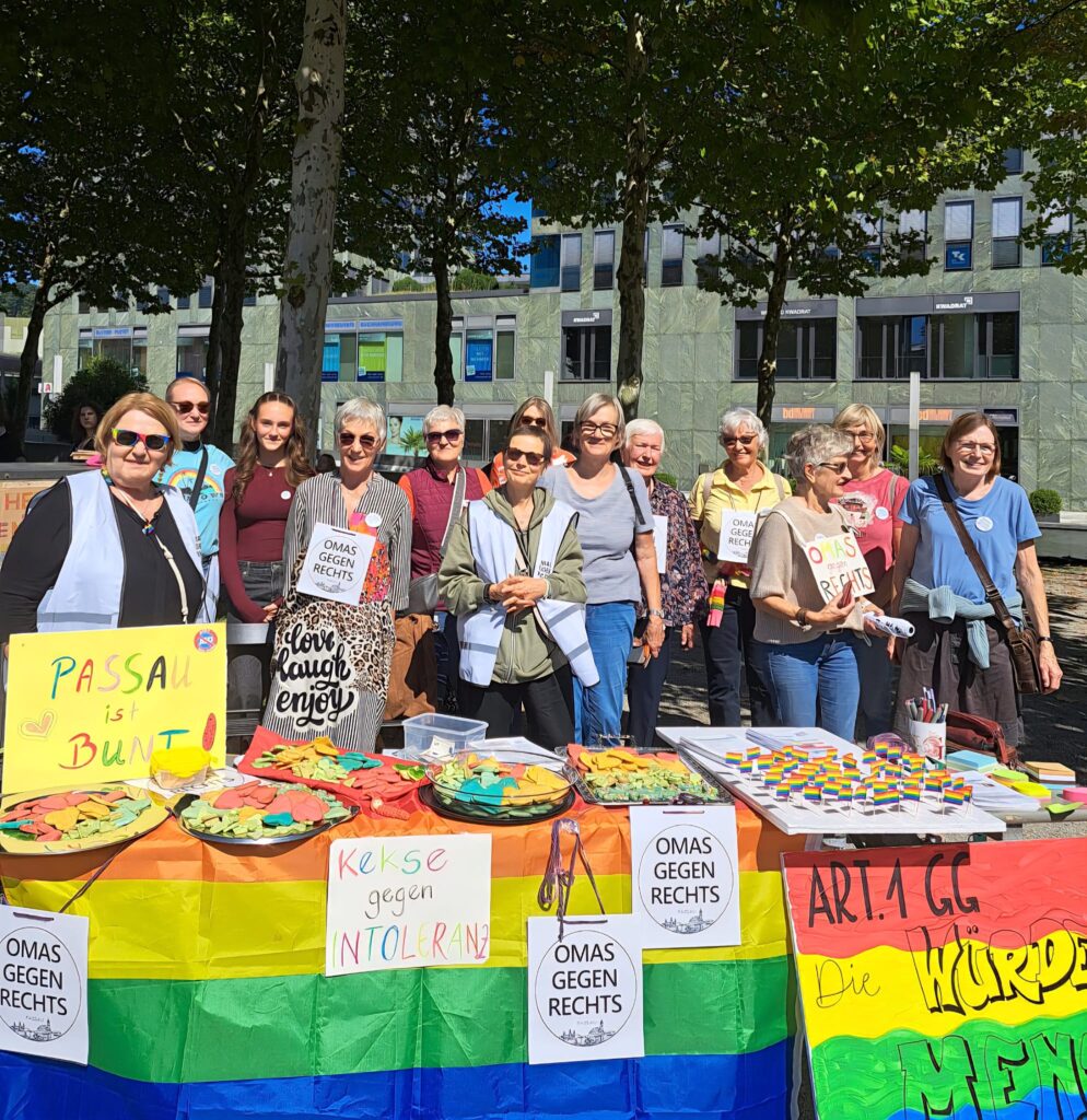DIe Omas Gegen Rechts Passau stehen hinter ihrem Regenbogenfarbenen Stand im Klostergarten Passau.